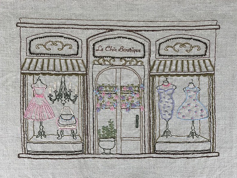 Puede incluir: Imagen bordada de un escaparate de boutique, "Le Chic Boutique", con vestidos en maniqu&iacute;es en los escaparates. La tienda tiene un toldo y adornos marrones, con una l&aacute;mpara de ara&ntilde;a y detalles florales. Los vestidos son rosas, azules y blancos.