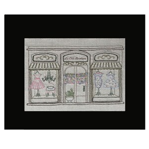 Puede incluir: Imagen bordada de un escaparate de boutique con el texto "Le Chic Boutique". La tienda presenta tres escaparates con vestidos en maniqu&iacute;es, una l&aacute;mpara de ara&ntilde;a y detalles florales. La paleta de colores incluye rosa, azul y verde sobre un fondo neutro.