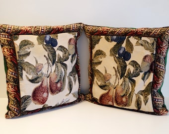 May include: Two decorative throw pillows with a cream-colored background featuring a repeating pattern of pears, leaves, and plums. The pillows have a green, brown, and gold border.