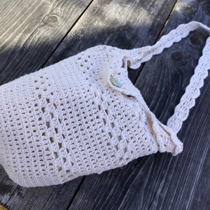 Peut inclure: Un sac fourre-tout en crochet de couleur crème avec une fermeture à bouton unique et une bandoulière en crochet.