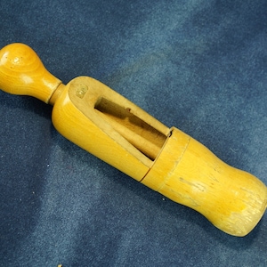 May include: A wooden shoe stretcher with a round knob on one end and a slot for inserting a shoe. The stretcher is made of light brown wood and has a natural finish.