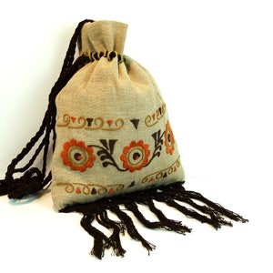 May include: A beige linen drawstring bag with brown tassels. The bag is decorated with embroidered orange and brown floral designs.