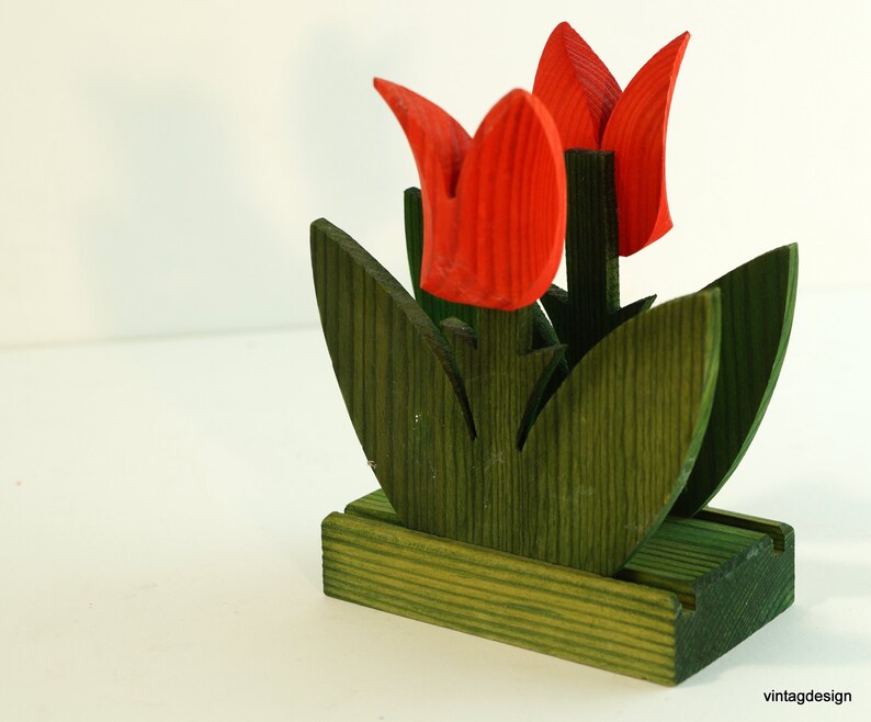 May include: A wooden napkin holder shaped like a bouquet of red tulips with green leaves. The holder has a rectangular base.