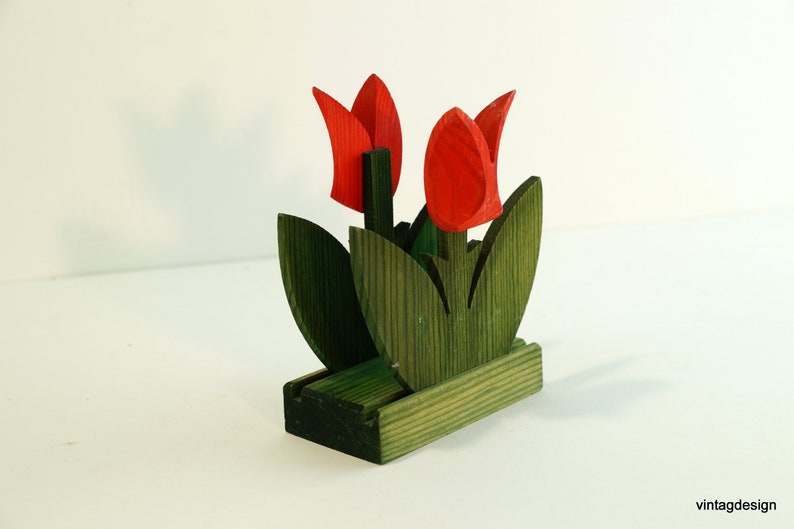 May include: Wooden napkin holder shaped like a bouquet of red tulips with green leaves.