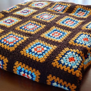 May include: A brown crocheted throw blanket with a granny square pattern in shades of blue, orange, yellow, and white.
