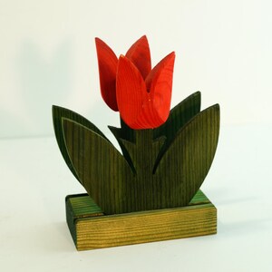 May include: Wooden napkin holder shaped like a bouquet of red tulips with green leaves. The holder has a rectangular base.