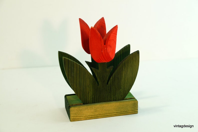 May include: Wooden napkin holder shaped like a bouquet of red tulips with green leaves. The holder has a rectangular base.