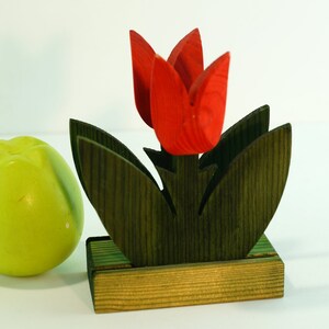 May include: Wooden napkin holder shaped like a red tulip with green leaves and a brown base.