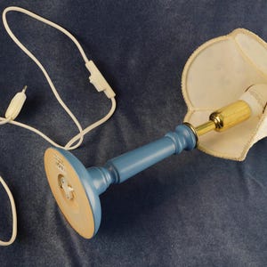 K&ouml;nnte beinhalten: Eine blaue Keramik-Tischlampe mit einem wei&szlig;en Stofflampenschirm. Die Lampe hat ein Kabel mit einem integrierten Schalter.
