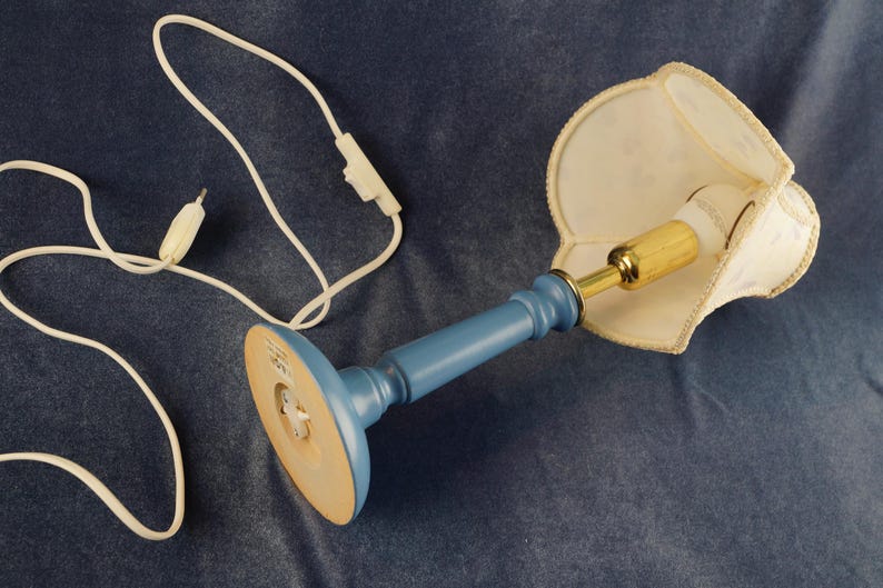 K&ouml;nnte beinhalten: Eine blaue Keramik-Tischlampe mit einem wei&szlig;en Stofflampenschirm. Die Lampe hat ein Kabel mit einem integrierten Schalter.