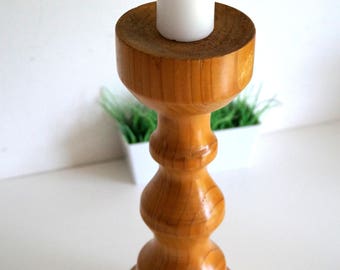 Puede incluir: Un candelero de madera con un diseño simple y elegante. El candelero tiene una base ancha y un tallo alto y delgado con una parte superior redondeada. El candelero está hecho de madera natural y tiene un acabado cálido y rústico.