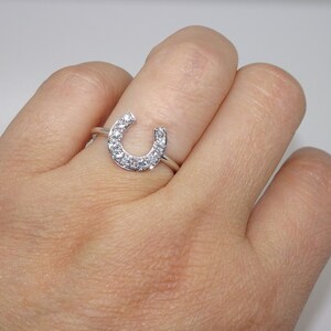 May include: A silver ring with a horseshoe design set with small clear cubic zirconia stones.