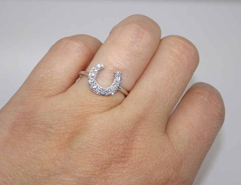 May include: A silver ring with a horseshoe design set with small clear cubic zirconia stones.