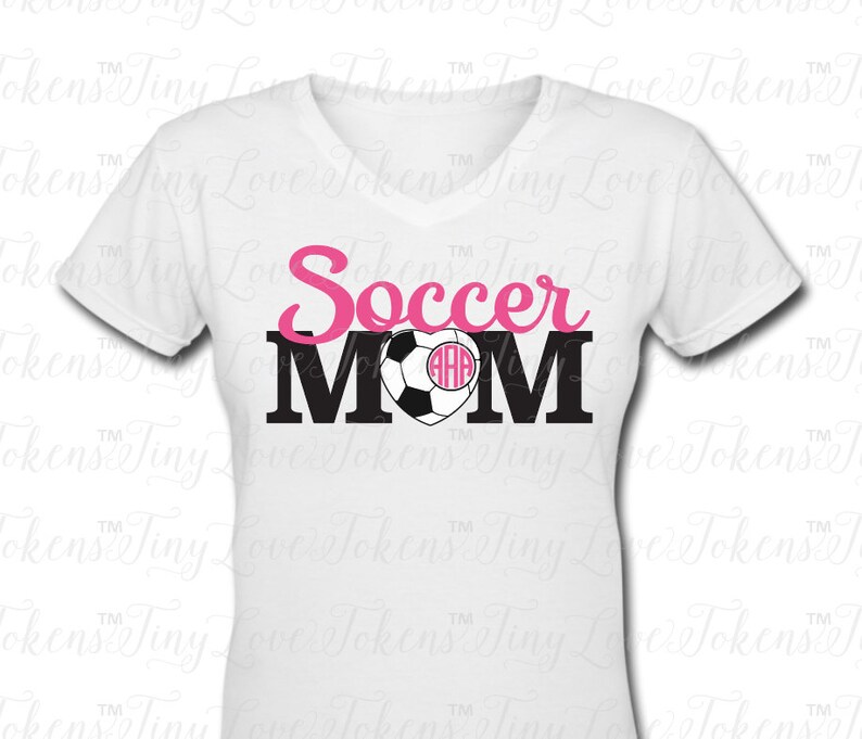 May include: White t-shirt with a pink and black design that says "Soccer Mom" with a soccer ball and a monogram in the heart.