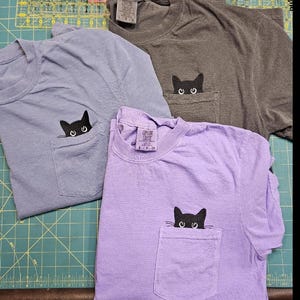 Embroidered black cat peeking out of pocket. Halloween Cat T-shirt.