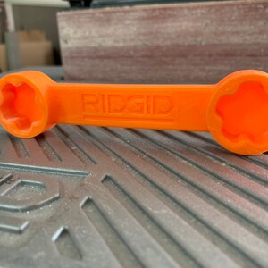 May include: An orange plastic wrench with a star-shaped opening on each end. The wrench is labeled "RIDGID".