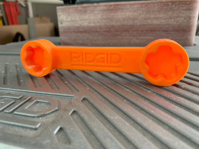 May include: An orange plastic wrench with a star-shaped opening on each end. The wrench is labeled "RIDGID".