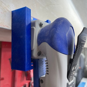 May include: A blue and gray power tool with a black handle and a blue and white wall mount. The tool has a black and white label that says "Sander Electric sander".