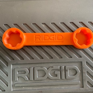 May include: An orange plastic wrench with a star-shaped opening on each end. The wrench is labeled "RIDGID" in the center.