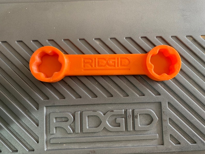 May include: An orange plastic wrench with a star-shaped opening on each end. The wrench is labeled "RIDGID" in the center.