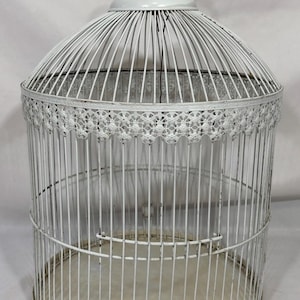 May include: A white metal birdcage with a dome-shaped top and a circular hanging ring. The structure features vertical wire bars and a decorative scalloped metal trim around the upper circumference, resting on a solid circular base plate.