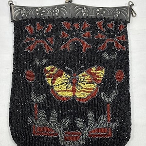May include: A vintage beaded handbag with a black background and a butterfly design. The butterfly has yellow and red wings. The bag has a silver-colored metal clasp and a beaded fringe at the bottom.