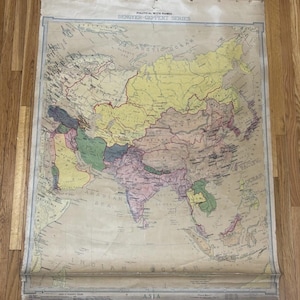 May include: A vintage map of Asia, featuring a detailed depiction of countries and geographical features. The map is printed on aged paper and includes the text "Political with Names" and "Denoyer-Geppert Series". The map is mounted on a wooden rod.