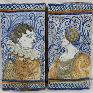 May include: Two rectangular ceramic tiles featuring hand-painted portraits of individuals in profile. The tiles display blue, white, and ochre color palettes with intricate swirling patterns, decorative borders, and detailed period-style clothing.