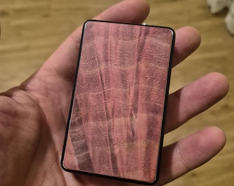May include: A rectangular object with a black frame and a flat, pinkish-brown wood grain inlay featuring a distinct, wavy, and textured pattern across the surface. The item has a smooth, polished finish and a clean, geometric, and symmetrical shape.