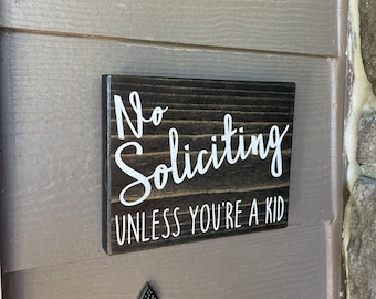 May include: A dark brown wooden sign with white text that reads "No Soliciting Unless You're a Kid".