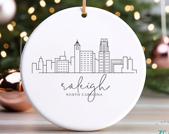Może przedstawiać: Biała ceramiczna ozdoba choinkowa z czarnym konturem panoramy Raleigh w Karolinie Północnej i tekstem "raleigh NORTH CAROLINA".