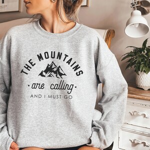 May include: Gray sweatshirt with black text that reads "The Mountains are calling. And I must go."  The text is in a semi-circle around a black silhouette of mountains.