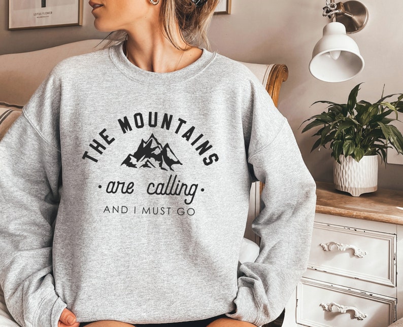 May include: Gray sweatshirt with black text that reads "The Mountains are calling. And I must go."  The text is in a semi-circle around a black silhouette of mountains.