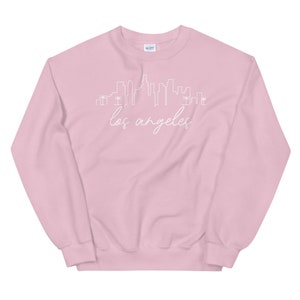 May include: A pink sweatshirt with a white outline of the Los Angeles skyline and the text "los angeles" in white cursive.