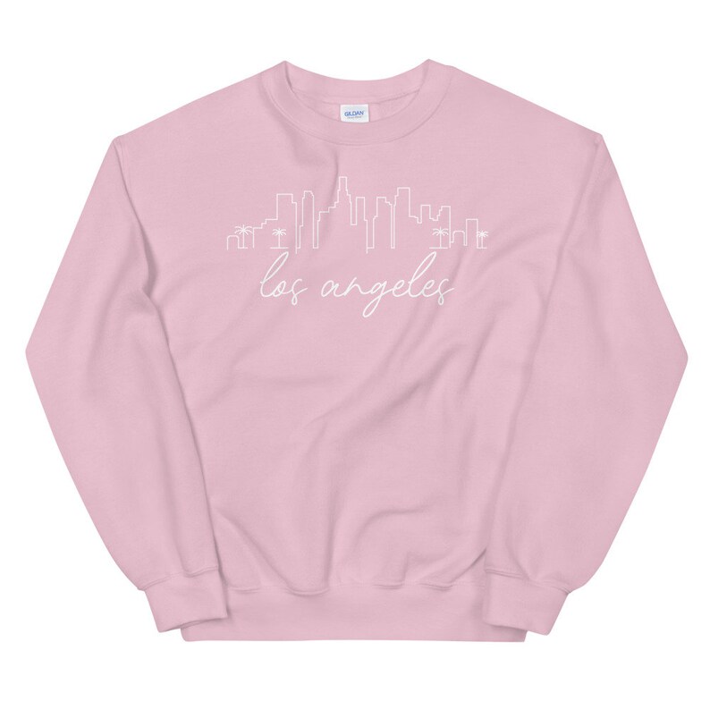 May include: A pink sweatshirt with a white outline of the Los Angeles skyline and the text "los angeles" in white cursive.
