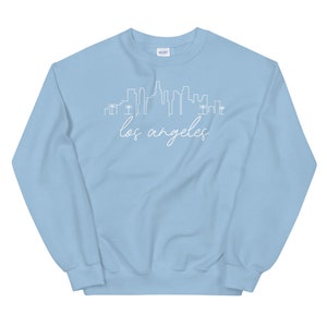 May include: Light blue sweatshirt with a white outline of the Los Angeles skyline and the text "los angeles" in white cursive.
