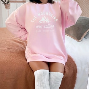 May include: A pink sweatshirt with the text "THE MOUNTAINS are calling. AND I MUST GO" in white. The text is surrounded by a mountain graphic.