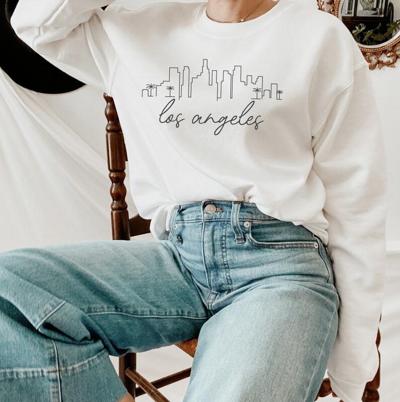 May include: A white sweatshirt with a black outline of the Los Angeles skyline and the text "los angeles" in cursive.