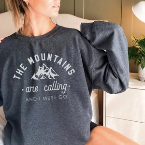 May include: A dark gray sweatshirt with the text "THE MOUNTAINS are calling. AND I MUST GO" and a graphic of mountains in white.