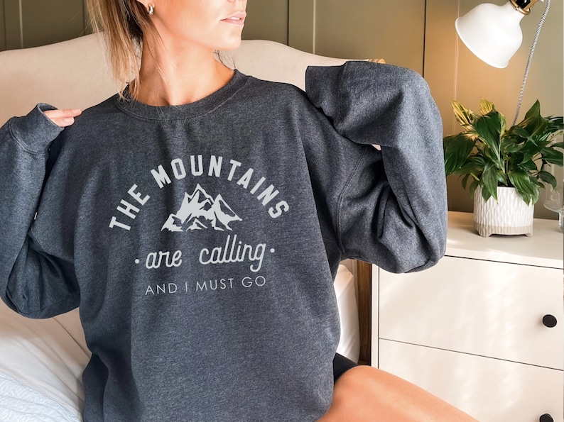May include: A dark gray sweatshirt with the text "THE MOUNTAINS are calling. AND I MUST GO" and a graphic of mountains in white.