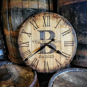 May include: A wooden clock with Roman numerals and a black metal frame. The clock is mounted on a wooden barrel and has the text "The Brewers Est. 2023" on the face.