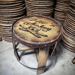 May include: A wooden stool with a round seat made from a repurposed whiskey barrel. The seat has a burnt-in design that says "Willie's Whiskey Bar".