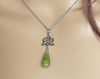 May include: A silver Celtic knot pendant necklace and matching earrings with green stone drops. The necklace and earrings are on a mannequin.