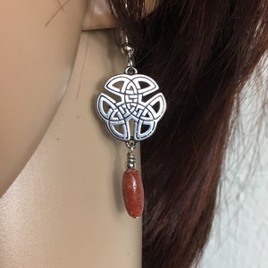 May include: Silver Celtic knot earrings with a dangling red coral bead.