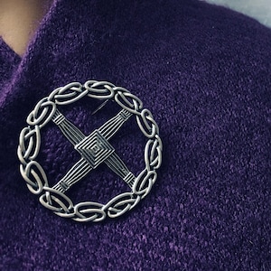May include: A silver circular brooch with a Celtic knot design. The brooch is worn on a purple knitted garment.