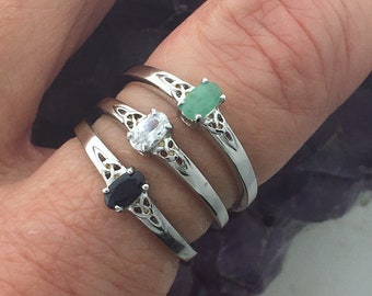 May include: Three silver Celtic knot rings with different colored gemstones. The top ring has a green gemstone, the middle ring has a white gemstone, and the bottom ring has a black gemstone.