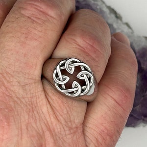 Könnte beinhalten: Ein silberner Ring mit einem keltischen Knotendesign. Der Ring wird an einem Finger getragen.