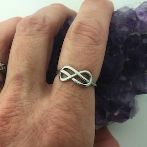 May include: A silver infinity symbol ring on a finger.