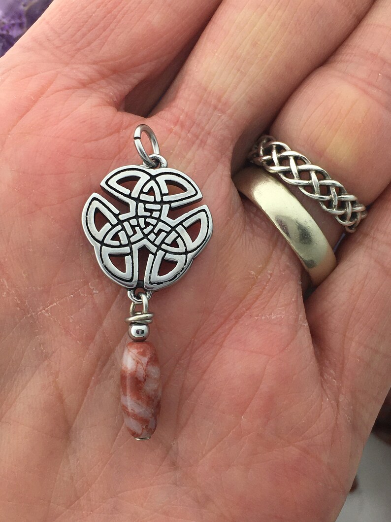 May include: Silver Celtic knot pendant with a red and white agate bead hanging from it.