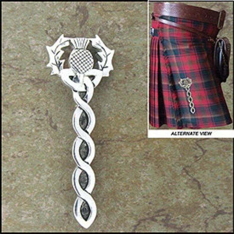 May include: Silver kilt pin with a Celtic knot design and a thistle emblem. The pin is shown against a textured background and an image of a kilt.